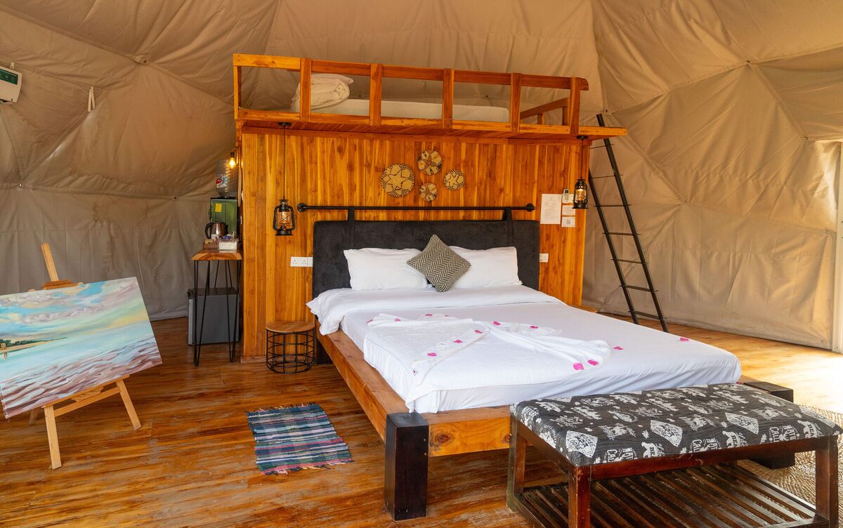 Inside a Family Garden dome at Cterra Saadani, with the loft rail and the bench at the foot of the bed