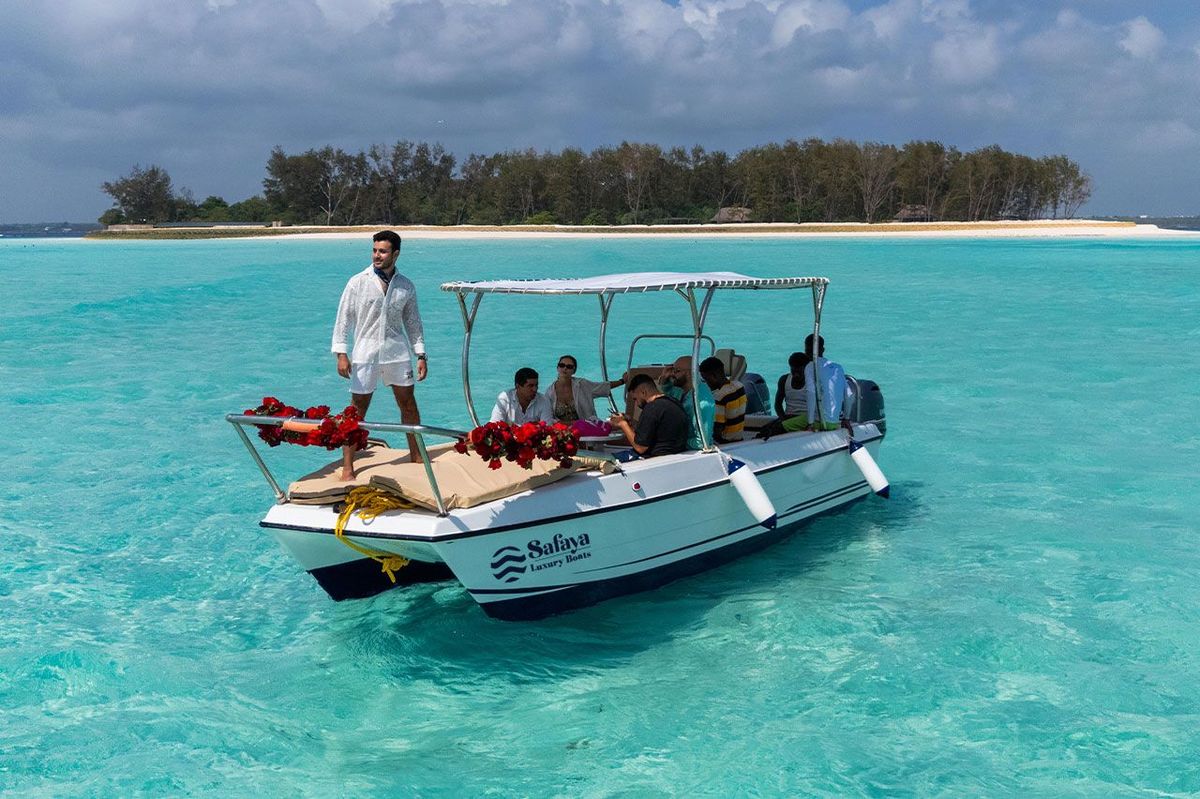 Le bateau privé mouillé près d’un banc de sable dans une eau turquoise limpide, les hôtes à bord sous l’auvent